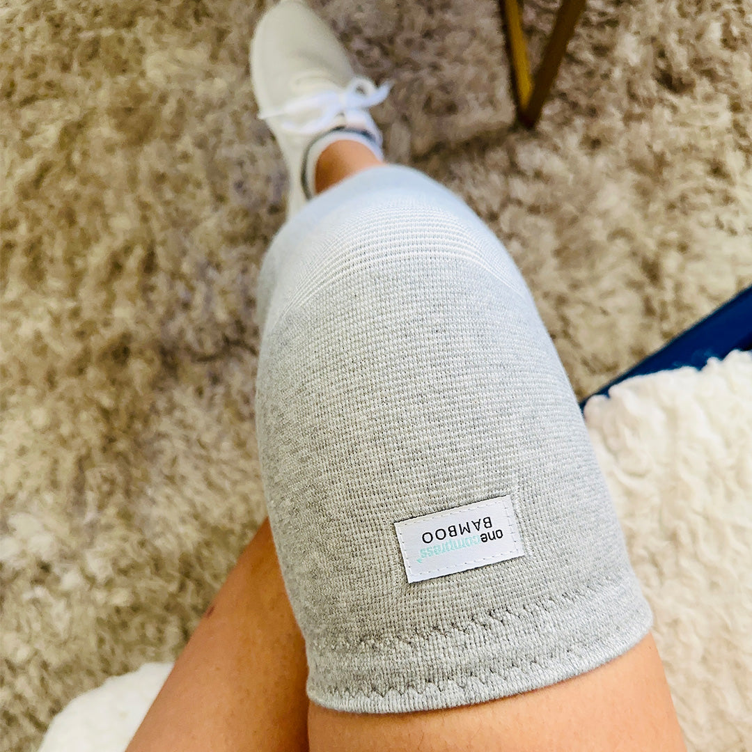 Person relaxing in bed wearing grey bamboo-infused compression socks for foot pain relief and improved circulation.
