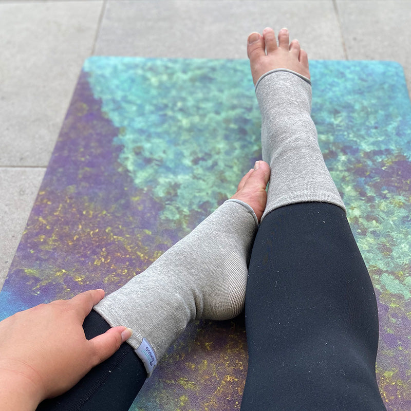 Person relaxing at home wearing grey compression knee sleeves for pain relief and improved circulation.